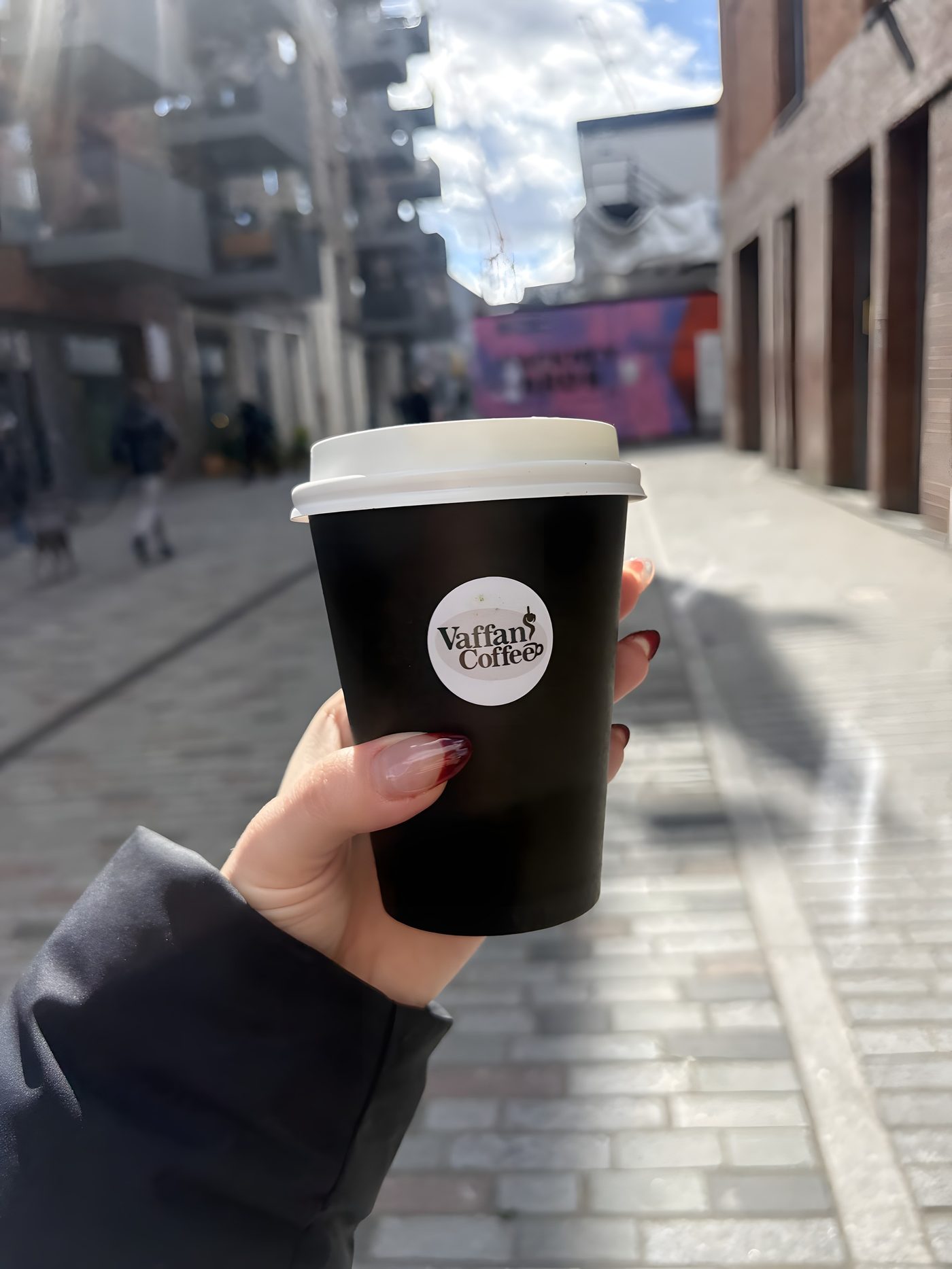 A Vaffancoffee takeaway cup held up on a sunlit Hackney Wick street